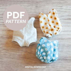 Op de afbeelding: Drie poppenoutfits worden getoond. Eén is wit, de tweede is wit met gele en oranje bloemen en de derde is lichtblauw met witte bloemen. De woorden "PDF PATTERN" staan in een cirkel bovenaan en "DIGITAL DOWNLOAD" onderaan.