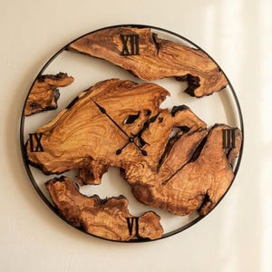 Puede incluir: Un reloj de pared redondo con una esfera de madera natural y un marco de metal negro. La esfera del reloj está hecha de piezas de madera de forma irregular con vetas visibles. Los números romanos negros marcan las horas. Las manecillas son negras.