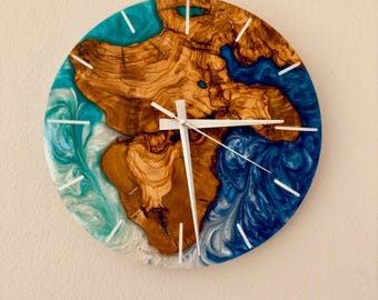 Può includere: Orologio da parete rotondo con un design unico. Il quadrante presenta una combinazione di legno naturale e resina blu, creando un contrasto sorprendente. Lancette e indicatori bianchi completano il design. L'orologio è montato su una parete di colore neutro.