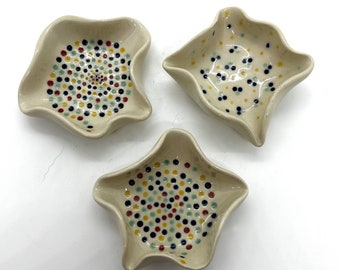 May include: Three small, white ceramic dishes with a wavy edge. Each dish has a different pattern of colorful dots in shades of blue, yellow, red, and green.