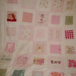 May include: A white quilt with a patchwork design. The quilt is made up of squares of different fabrics, including pink, white, and floral patterns. The quilt has a white border and is decorated with various embroidered designs, including stars, flowers, and animals.