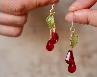 May include: A pair of dangle earrings with red teardrop-shaped glass beads and green leaf charms.