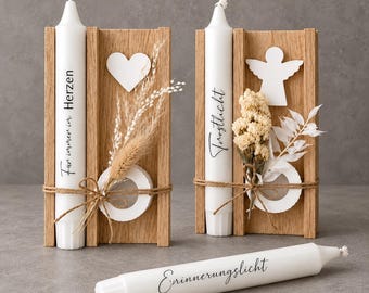 Op de afbeelding: Twee houten kaarsenhouders met witte kaarsen, versierd met gedroogde bloemen, een wit hart of engel-uitsparing en touw. De kaarsen dragen de teksten "Für immer im Herzen", "Trostlicht" en "Erinnerungslicht".