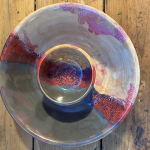 May include: A ceramic serving dish with a smaller bowl in the center. The dish is decorated with a colorful glaze in shades of red, blue, and brown.