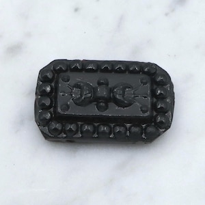 May include: Black glass button with a raised design of a stylized butterfly. The button is surrounded by a beaded border.