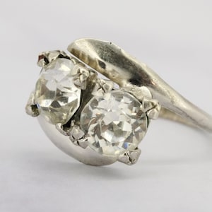 Op de afbeelding: Een zilveren ring met twee heldere, gefacetteerde stenen gezet in een gedraaide band.