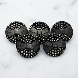 May include: Five black buttons with a raised bow design and a sparkly finish. The buttons are round and have a diameter of approximately 2.5 cm.