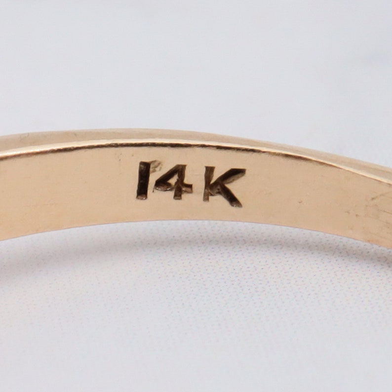 May include: Close-up of the inside of a gold ring with the inscription "14K" on the band.