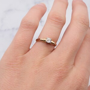 May include: A gold band engagement ring with a single round diamond set in the centre. The band is decorated with a series of small, raised circles.