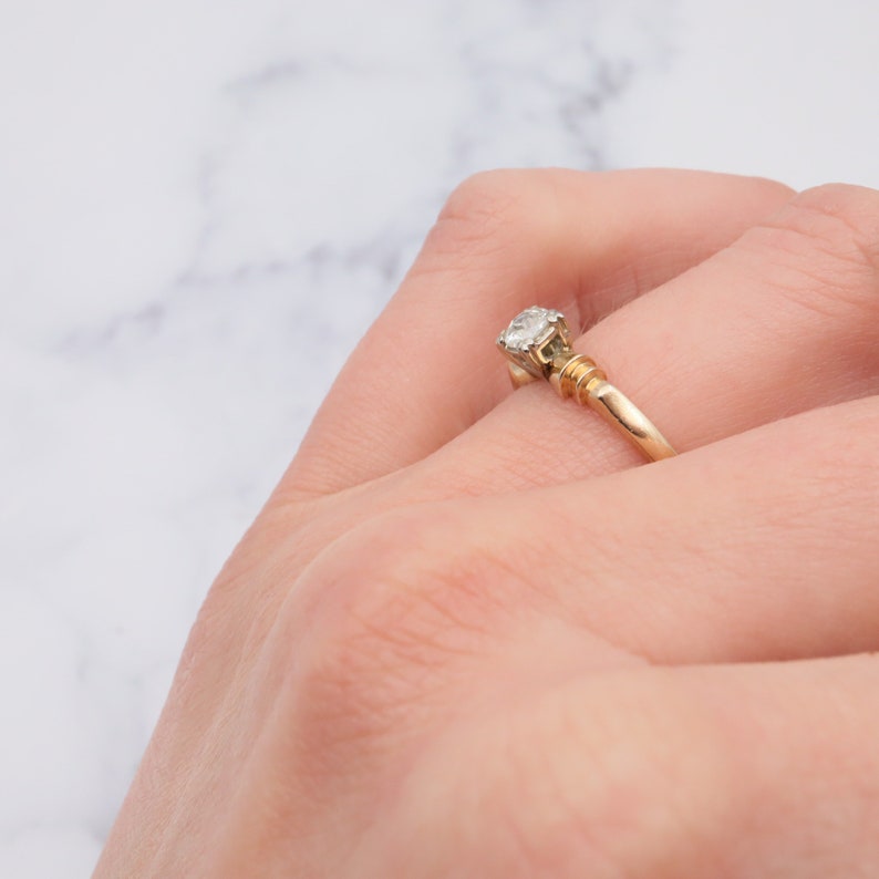 May include: A gold band engagement ring with a single round diamond set in a prong setting.