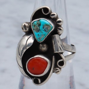 May include: A silver ring with turquoise and coral stones. The ring has a unique design with a leaf-like shape and intricate details.