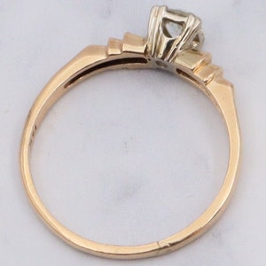 May include: A gold engagement ring with a single round diamond set in a prong setting. The band is a simple, thin band with a slightly rounded edge.