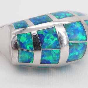 May include: A silver ring with a blue and green opal inlay. The opal is set in a geometric pattern.