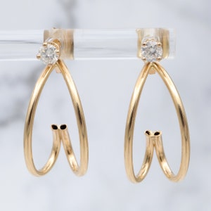 May include: A pair of gold hoop earrings with a single diamond in each hoop. The hoops are double-layered and have a heart shape.