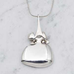 May include: A silver pendant necklace with a unique abstract design. The pendant is made of smooth, polished silver and has a geometric shape.