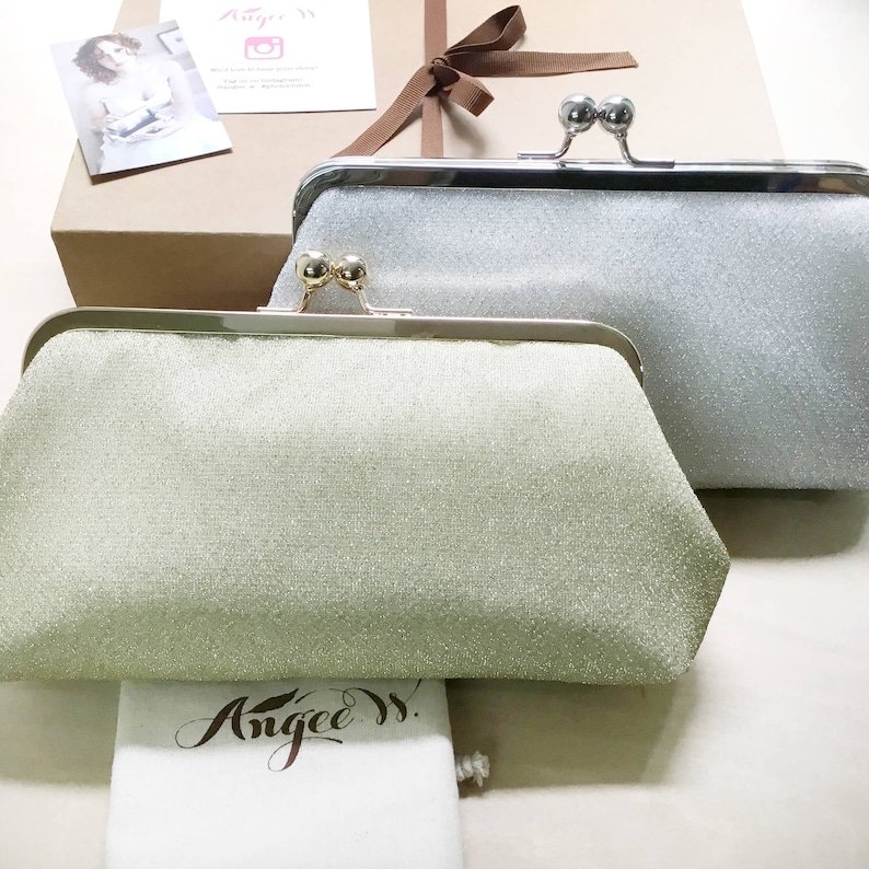 A light gold and a silvery shimmery clutch placed side by side against the dust bag and kraft paper gift box tied with a ribbon