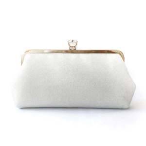 A shimmery silver clutch bag in silver mounted on a double metal frame in light gold tone adorned with a centre 26mm diameter crystal in the centre.