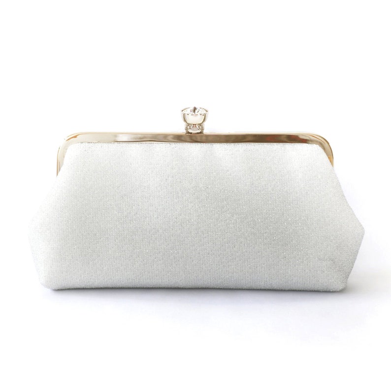 A shimmery silver clutch bag in silver mounted on a double metal frame in light gold tone adorned with a centre 26mm diameter crystal in the centre.