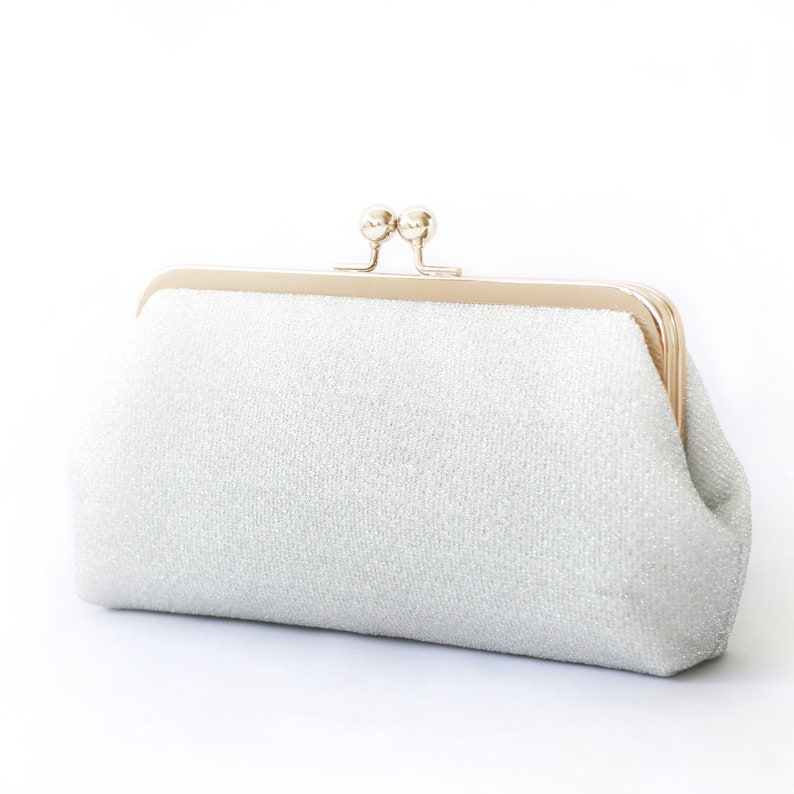 A shimmery silver clutch bag in silver mounted on a double metal frame in light gold tone adorned with kisslock 2-ball clasp in the centre