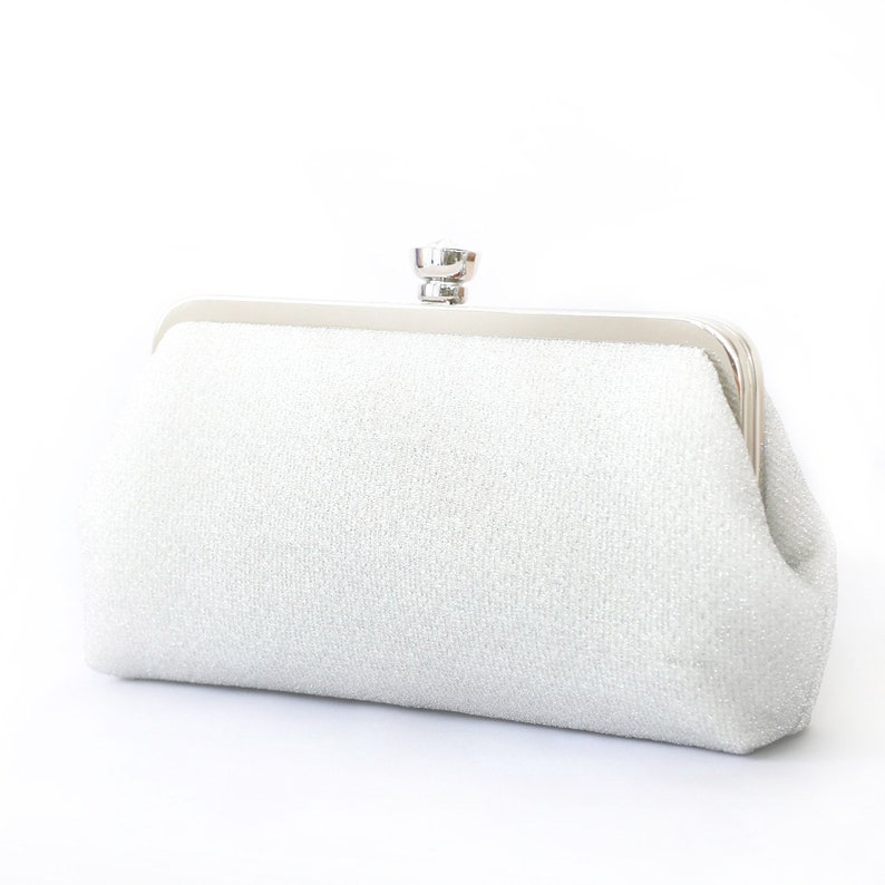 A shimmery silver clutch bag in silver mounted on a double metal frame in silver  tone adorned with a centre 26mm diameter crystal in the centre.