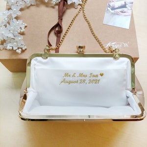 Puede incluir: Un bolso de mano dorado con forro de sat&eacute;n blanco y una cadena dorada. El bolso tiene una inscripci&oacute;n personalizada que dice "Mr. & Mrs. Ina August 28, 2021" con un peque&ntilde;o coraz&oacute;n.