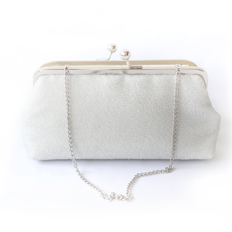 A shimmery silver clutch bag in silver mounted on a double metal frame in silver tone adorned with kisslock 2-ball clasp in the centre. Also featuring a 15 inch long metal chain hanging from the bag.