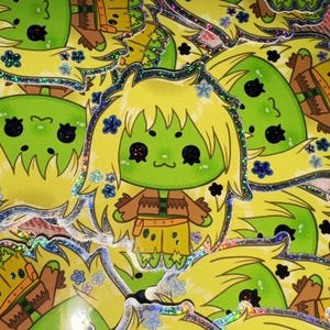 May include: A collection of stickers featuring a cartoon character with green skin, yellow hair, and a small smile. The character wears a brown top and yellow shorts. The stickers have a glittery, holographic border and are decorated with small blue and black flower accents.