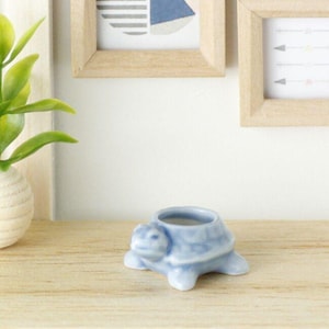 May include: A small blue ceramic turtle planter. The planter has a glazed finish and is shaped like a turtle with its head and legs visible.