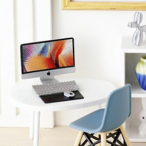 Puede incluir: Un escritorio blanco en miniatura con una computadora plateada, un teclado y un ratón. Una silla azul se encuentra junto al escritorio. El escritorio está sobre un suelo blanco.