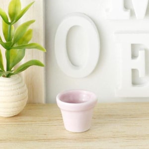 May include: A small, light pink ceramic planter pot. The pot is approximately 5 cm tall and has a slightly flared rim.