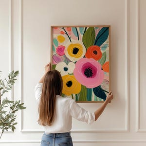 May include: A framed floral art print featuring a vibrant bouquet of stylized flowers in shades of pink, yellow, orange, and white, with green leaves. The artwork is set against a light background and framed in a natural wood frame.