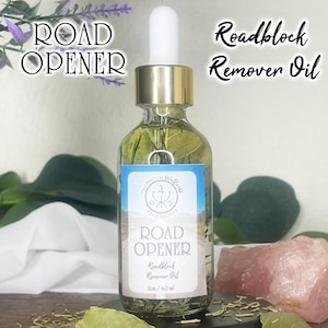 May include: A clear glass bottle with a gold cap and white dropper, filled with a green liquid and herbs. The label reads "ROAD OPENER Roadblock Remover Oil". The text "The Mystical Wellness Apothecary" is also visible. The bottle is 2 oz / 60 ml.