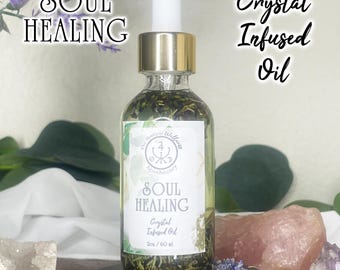 May include: A clear glass bottle with a gold cap and white dropper, filled with green herbs and oil. The label reads "SOUL HEALING Crystal Infused Oil". The bottle is on a black stand, with crystals and flowers in the background. The text "SOUL HEALING" and "Crystal Infused Oil" are also visible.