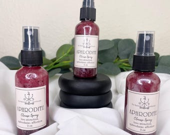 May include: Three bottles of Aphrodite Cleanse Spray, each with a black cap and a label. The bottles are filled with a reddish liquid. The labels read "Aphrodite Cleanse Spray, love attraction, aphrodisiac, affection, 2 oz."