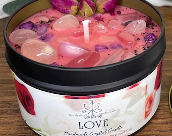 May include: A handmade crystal candle in a black tin, featuring a pink wax embedded with rose quartz and other crystals. The candle is topped with dried rose buds. The label reads "LOVE" and "Sweet Strawberry & Jasmine fragrance Oil."