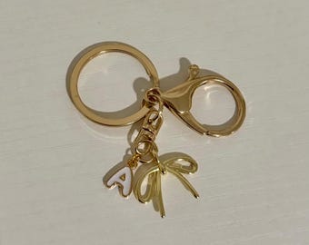 Peut inclure: Un porte-clés doré avec un grand anneau, un mousqueton et un charme avec une lettre A blanche et un nœud doré.