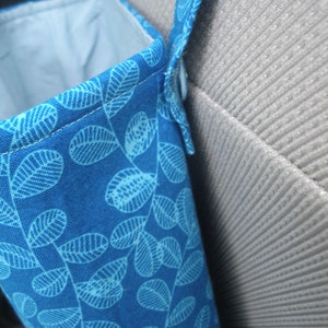 May include: A blue fabric car organizer with a white leaf pattern. The organizer has a strap to hang it on the back of a car seat.