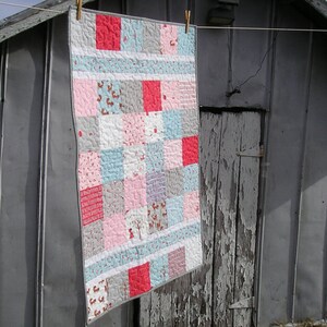 May include: A patchwork quilt with a variety of pink, blue, gray, and white fabrics. The quilt is made up of squares and rectangles, and it has a simple, modern design.