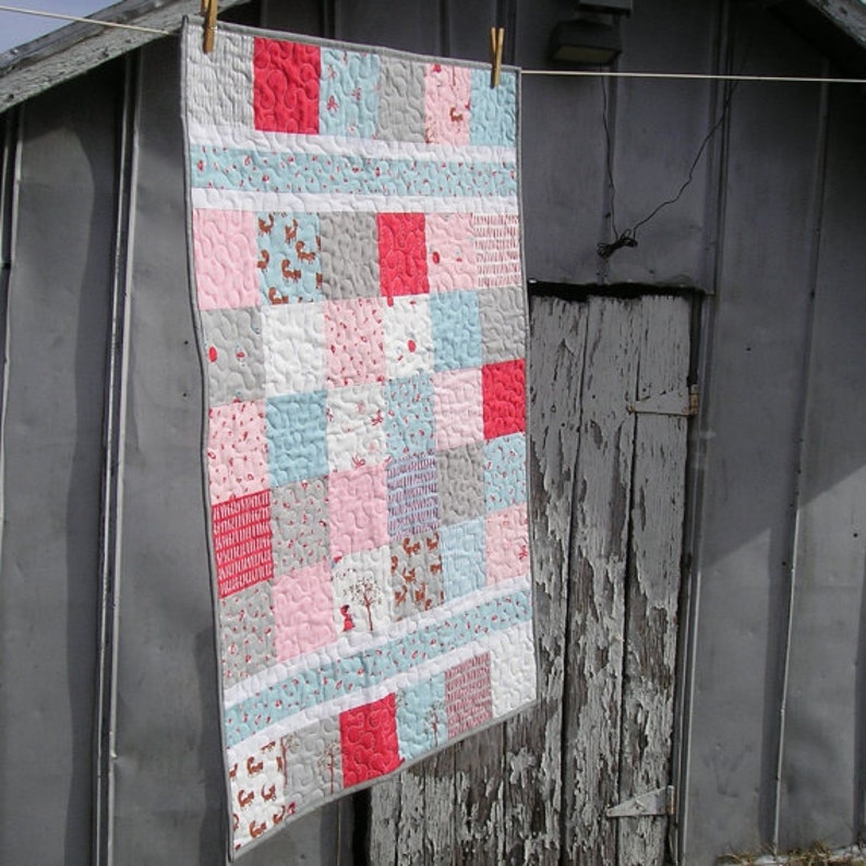 May include: A patchwork quilt with a variety of pink, blue, gray, and white fabrics. The quilt is made up of squares and rectangles, and it has a simple, modern design.