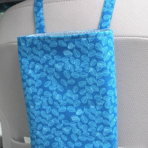May include: A blue fabric car trash bag with a white leaf pattern. The bag hangs from the headrest of a car seat.