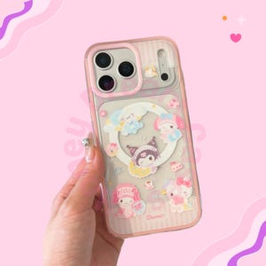 Op de afbeelding: Transparante telefoonhoes met een roze rand en een ontwerp met stripfiguren. De hoes heeft een transparante achterkant met een roze streepjespatroon en een cirkelvormig ontwerp met stripfiguren. De hoes wordt door een hand vastgehouden.