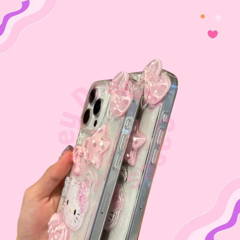 May include: Clear phone case with pink bow and star embellishments. The case features a Hello Kitty design and is decorated with glitter. The case is held against a pink background.
