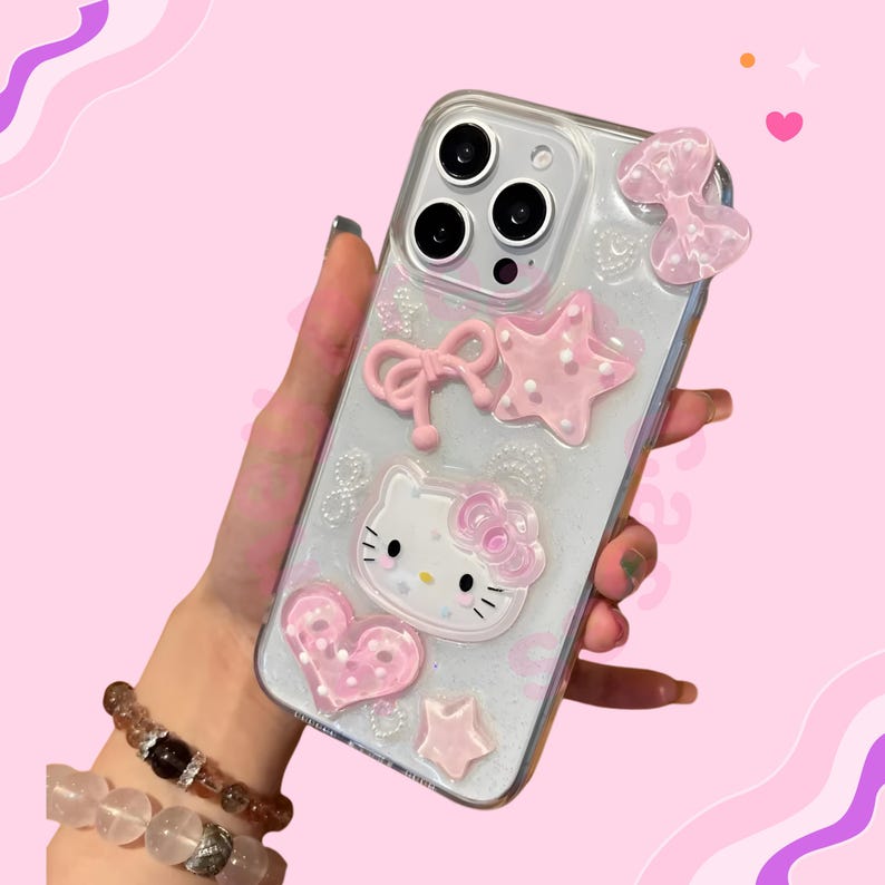 May include: Clear phone case decorated with pink bows, stars, and a heart. The case features a Hello Kitty design with a pink bow. The case is held in a hand against a pink background.