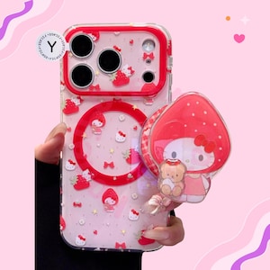 May include: Clear phone case with a red border and a strawberry and Hello Kitty design. The case has a matching pop-socket with a Hello Kitty strawberry design and a small teddy bear. The case has the text "Y CASE".