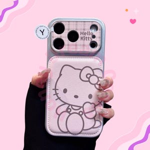 K&ouml;nnte beinhalten: Eine rosa Handyh&uuml;lle mit einem Hello Kitty-Design. Die H&uuml;lle hat eine hellrosa lederartige Textur mit einer Hello Kitty-Illustration. Der obere Teil hat ein Karomuster und die Worte "Hello Kitty".