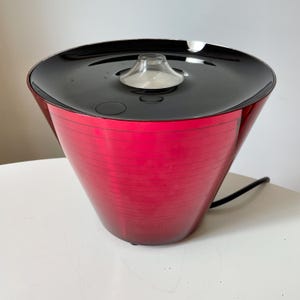 Può includere: Una tazza di ceramica bianca con manico nero e la scritta "But First, Coffee" in grassetto nero. La tazza si staglia su uno sfondo sfocato, evidenziando il suo design pulito.