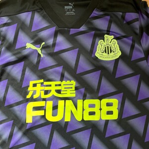 Puede incluir: Camiseta de f&uacute;tbol negra y morada con un patr&oacute;n geom&eacute;trico. La camiseta presenta el logo de Puma en verde lima, junto con el texto "乐天堂 FUN88" en amarillo. Tambi&eacute;n es visible el escudo del Newcastle United.