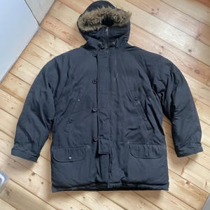 Puede incluir: Parka de invierno negra con capucha forrada de piel. La chaqueta tiene cierre de cremallera, parte delantera abotonada y dos bolsillos delanteros. La parka está diseñada para climas fríos y está hecha de un material duradero y resistente al agua.