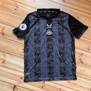 May include: A black and blue soccer jersey with a patterned design. The jersey has a V-neck collar and short sleeves. The team logo is visible on the chest and the Premier League logo is on the left sleeve.