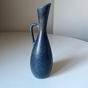 Könnte beinhalten: Eine blaue Keramikvase mit Henkel. Die Vase hat eine gesprenkelte Textur und eine ausgestellte Oberseite. Goldakzente sind in der Nähe der Oberseite sichtbar. Die Vase ist etwa 20 cm hoch.